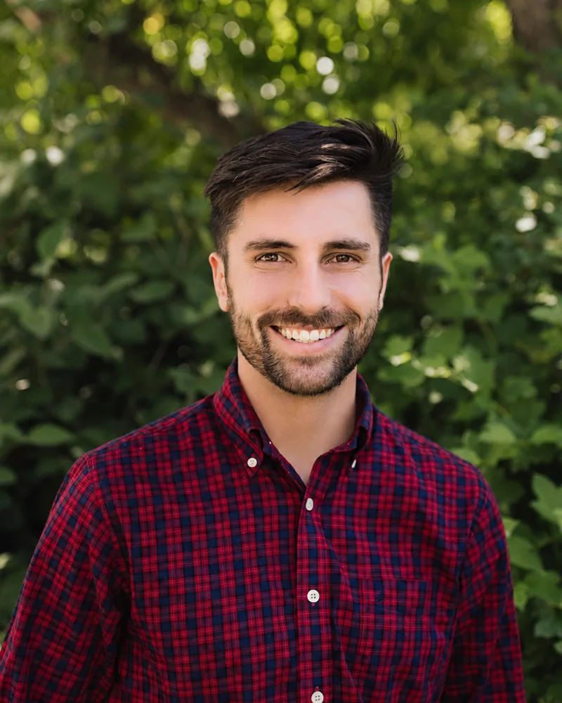 Jack Staples, founder of For Purpose Labs, smiling outdoors in front of green foliage